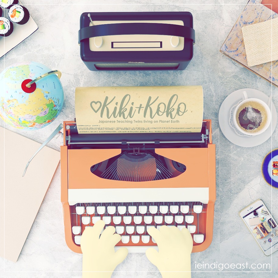 A vintage peach typewriter on a marble tabletop, presumably being typed on by Japanese teacher, Kiki or Koko. A journal entry is being typed onto parchment whilst the logo for ♡Kiki+Koko™, Japanese Teaching Twins living on Planet Earth. To the left is a miniature globe, sushi, and a notebook. To the other side is tea, books, and more sushi. In the lower right hand corner, you can see a recursive image on the smart phone, monitoring the camera image.